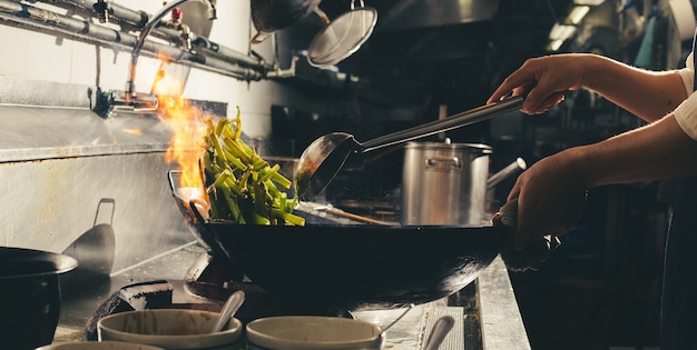 Chef-kok roerbak bezig met koken in de keuken. Chef roerbak het eten in een koekenpan, rook en spetter de saus in de keuken.