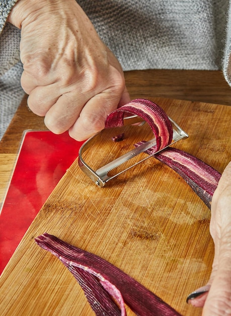 Chef-kok snijdt plakjes wortel van drie kleuren in de keuken op een houten bord