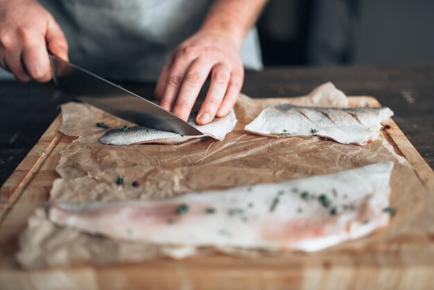 Chef-kok snijdt rauwe visplakken op houten snijplank