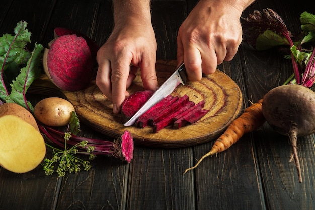 Chef-kok snijdt rode bieten in kleine stukjes op een snijplank in de keuken voordat hij een vegetarische maaltijd bereidt