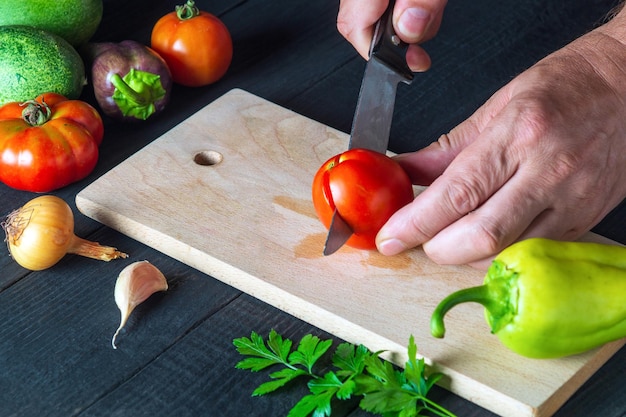 Chef-kok snijdt rode tomaat in restaurantkeuken voor salade Close-up van handen van kok tijdens het werk