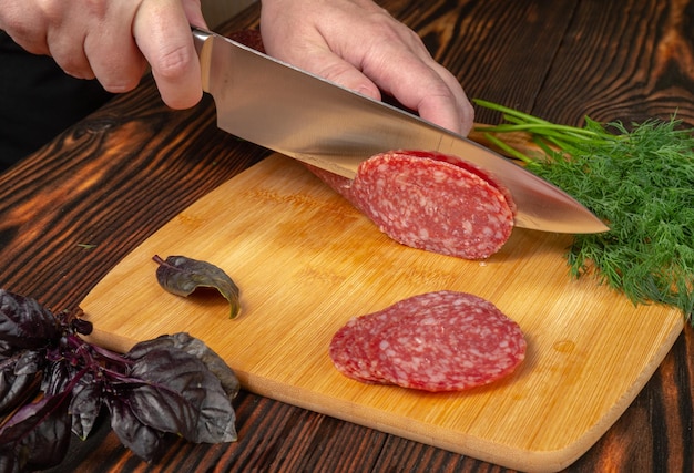 Foto chef-kok snijdt salami op een donkere houten tafel close-up