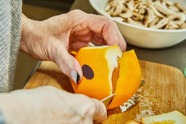 Chef-kok snijdt sinaasappels om salade met courgettesinaasappelen en salami Franse gastronomische keuken op een houten achtergrond te bereiden