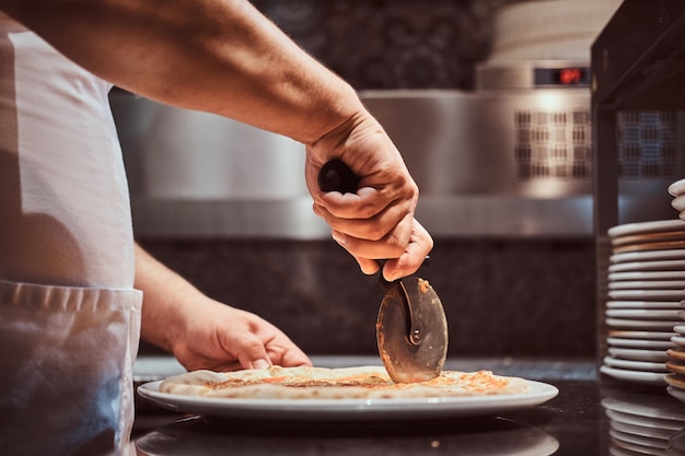 Chef-kok snijdt smakelijke pizza met speciaal mes in de keuken.