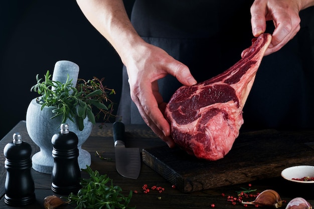 Chef-kok steak beef Mans handen houden rauwe steak Tomahawk op rustieke houten snijplank op zwarte achtergrond Koken recepten en eten concept Selectieve aandacht