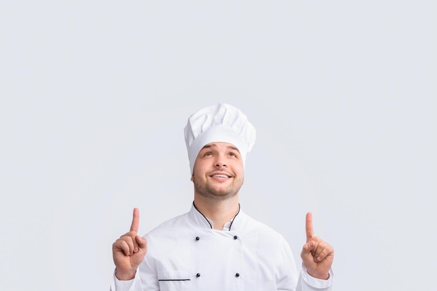 Chef-kok wijst met zijn vingers omhoog en staat op een witte achtergrond.