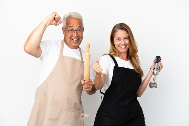 Chef-koks van middelbare leeftijd paar geïsoleerd op een witte achtergrond vieren een overwinning in winnaar positie