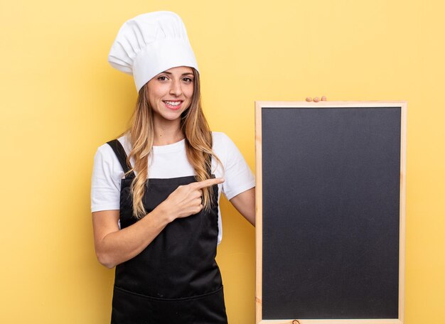 Chef-kokvrouw die vrolijk lacht, zich gelukkig voelt en naar de zijkant wijst. schoolbord menu concept