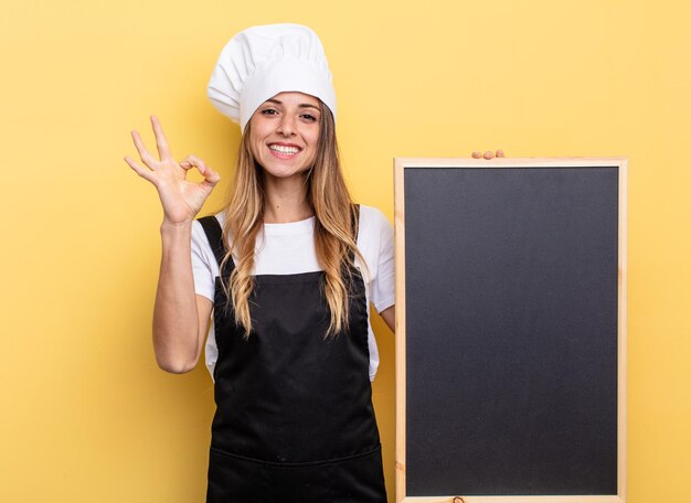 Chef-kokvrouw die zich gelukkig voelt, goedkeuring toont met een goed gebaar. schoolbord menu concept