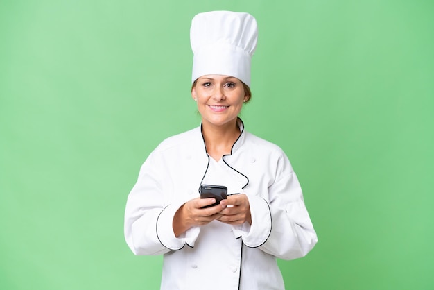 Chef-kokvrouw van middelbare leeftijd over geïsoleerde achtergrond die een bericht verzendt met de mobiel