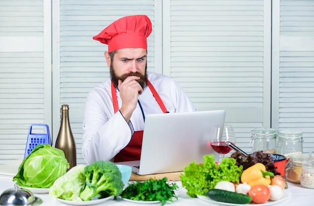 Chef laptop read culinary recipes Culinary school Hipster in hat and apron learning how to cook online Culinary education online Elearning concept Man chef searching internet recipe cooking food