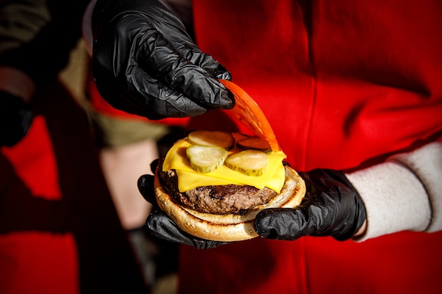 Lo chef prepara un hamburger con guanti neri. raccoglie gli ingredienti