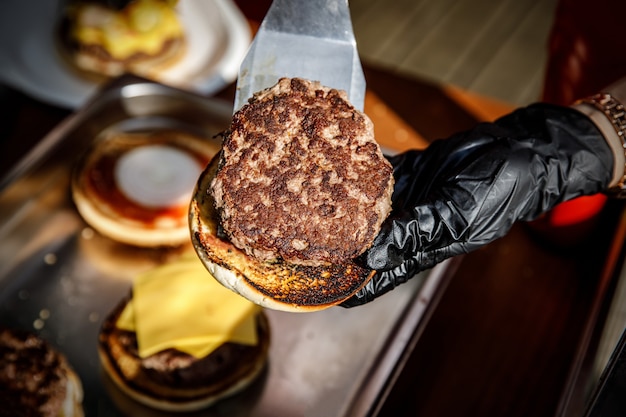 Chef makes a burger in black gloves. Picks up ingredients