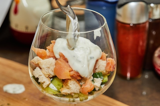 Chef makes Summer salad in glass of salmon cucumbers croutons herbs and fresh cream Elegant Summer Fusion