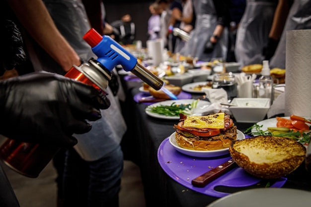 Foto chef che prepara hamburger di manzo sciogliere il formaggio su un panino con hamburger con un bruciatore culinario per hamburger nella cucina di un ristorante