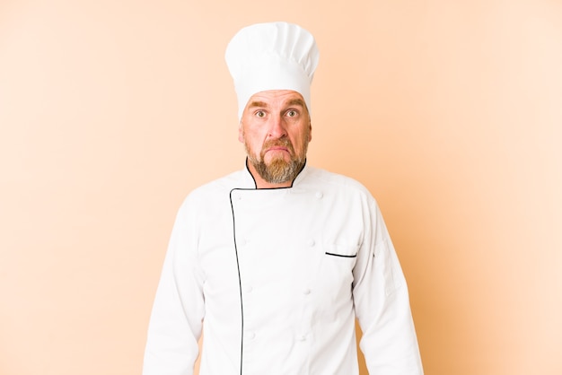 Chef man isolated on beige shrugs shoulders and open eyes confused.