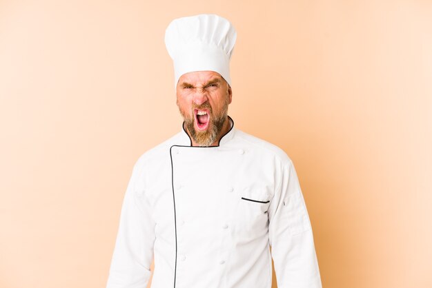 Chef man isolated on beige wall screaming very angry and aggressive.