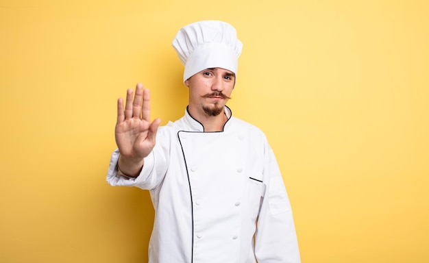 Мужчина шеф-повар выглядит серьезным, показывая открытую ладонь, делая стоп-жест