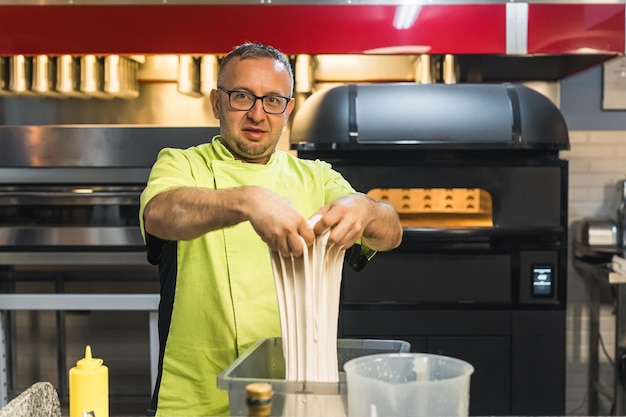 Chef met bril en uniform die het deeg in de bakkerij keuken kneden