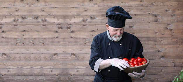 Chef old in uniform with fresh vegetables on a wooden bacground