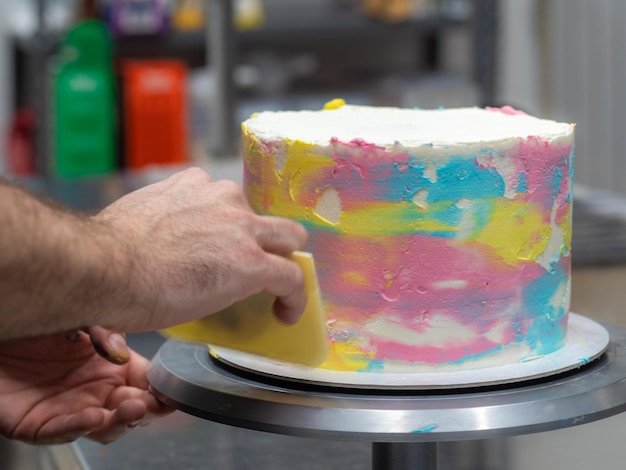 Chef pastry designer confectioning a frosted 3 floor layered cake decorated with pastel creamy colors