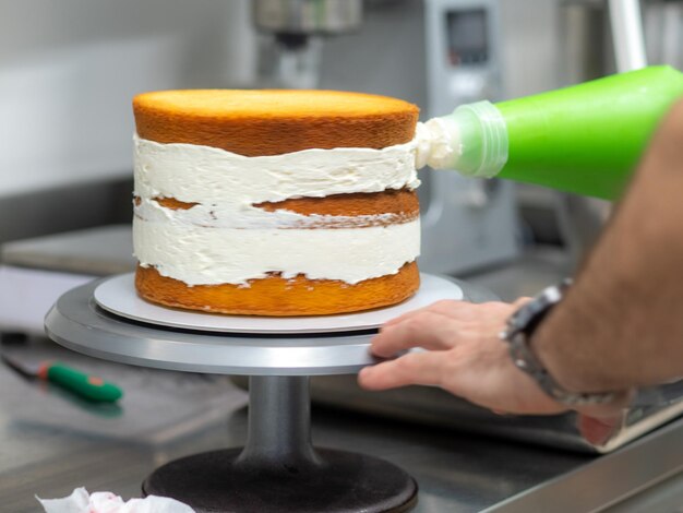 Foto chef pasticcere che prepara una torta a strati glassata a 3 piani farcita con fragole e crema al burro montata