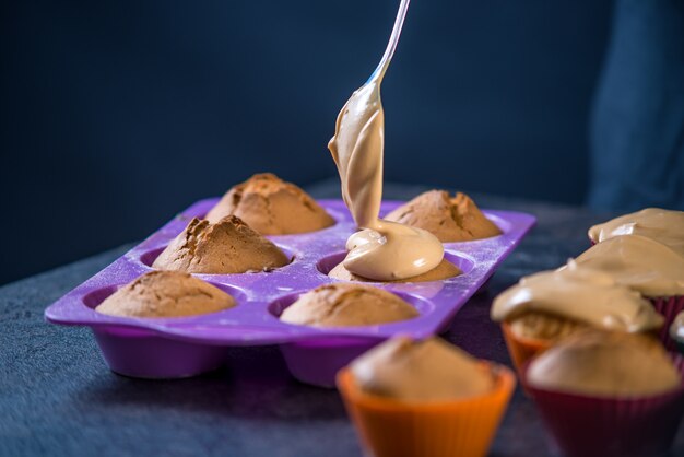 Chef pastry is pouring cream on freshly prepared cupcakes