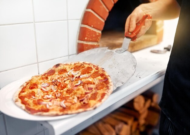 Foto chef che mette la pizza dalla buccia al piatto in una pizzeria