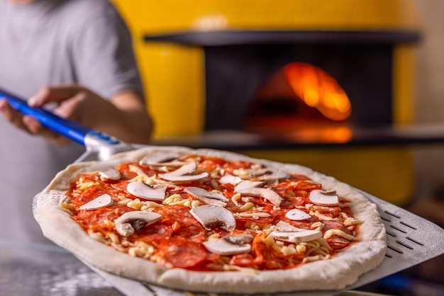 Photo chef placing the pizza in the hot oven to be baked the chef prepares pizza with