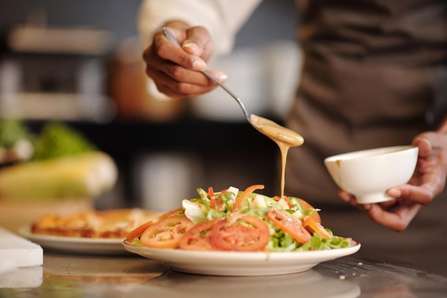 Chef pouring dressing on vegetable salad