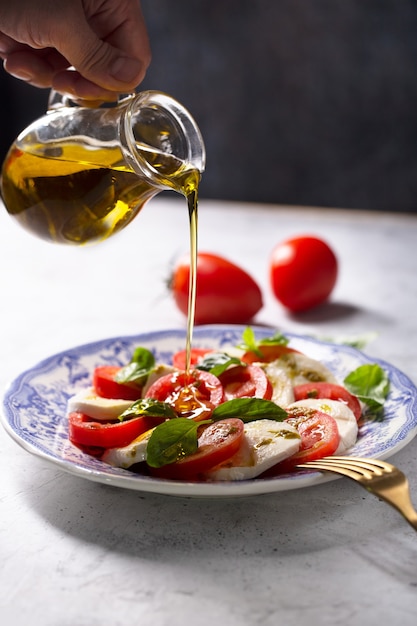 Chef pouring olive oil on a caprese salad. Italian famous salad with fresh tomatoes, mozzarella cheese and basil