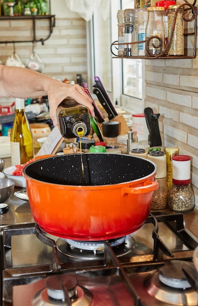 Foto chef che versa l'olio d'oliva nella padella sulla stufa a gas