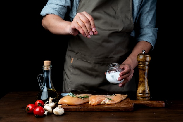 Chef pouring salt on chicken breast