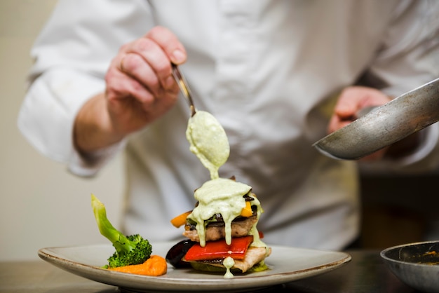 Photo chef pouring sauce over meal