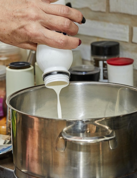 Chef pours cream from a bottle into a pan on a gas stove