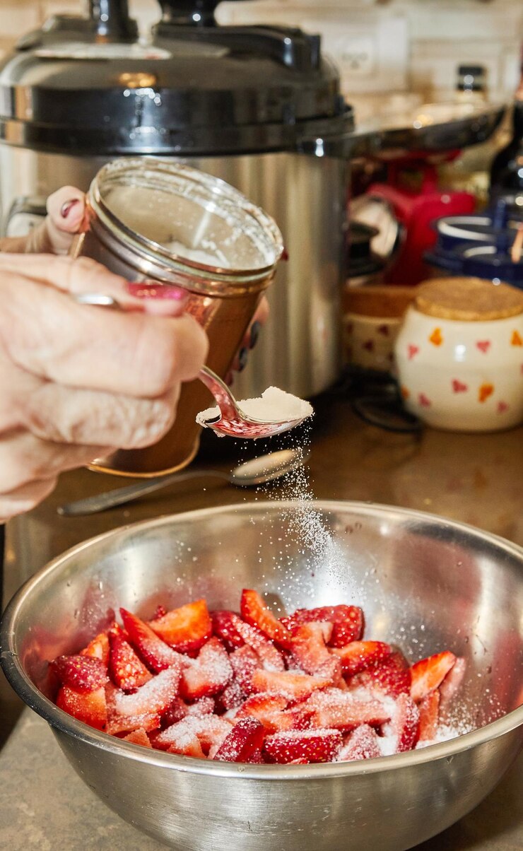 Photo chef pours sugar and spoons into sliced strawberries for dessert