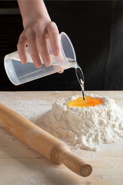 Photo chef pours water into flour with an egg