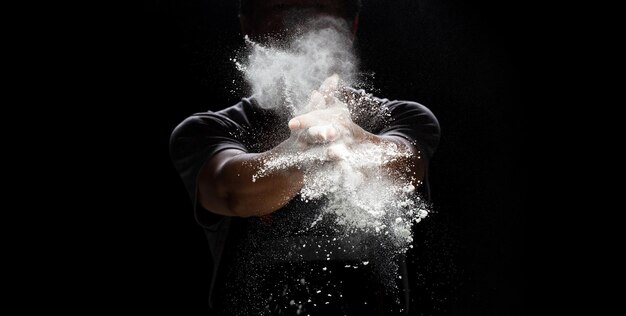 Chef prepare white flour dust for cooking bakery food Elderly man Chef clap hand white flour dust explode fly in air Flour stop motion in air with freeze high speed shutter black background
