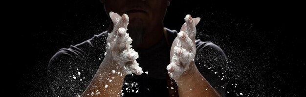 Chef prepare white flour dust for cooking bakery food Elderly man Chef clap hand white flour dust explode fly in air Flour stop motion in air with freeze high speed shutter black background