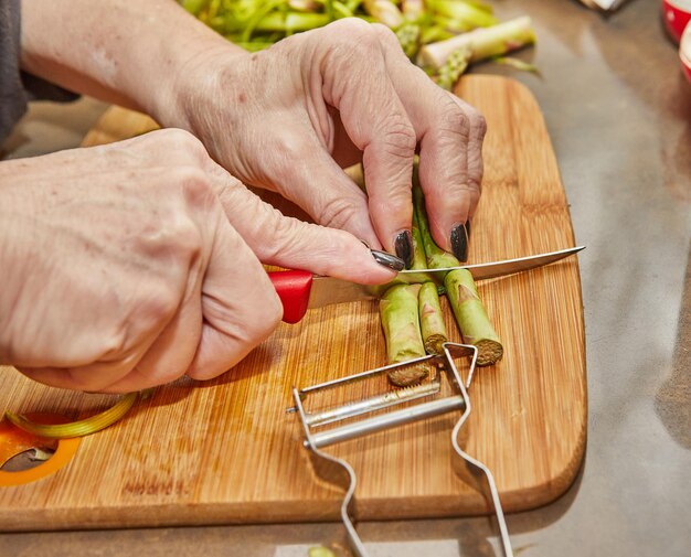 Chef prepares Asparagus in the kitchen on wooden board according to recipe from the Internet