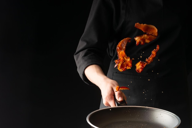 The chef prepares bacon roasting slices of bacon on a black background horizontal photo menu recipe book restaurants healthy and tasty food