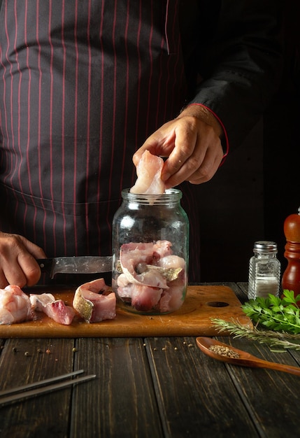 Photo the chef prepares fresh carp fish the cook hand puts a fish steak into a jar for pickling working environment in a restaurant kitchen