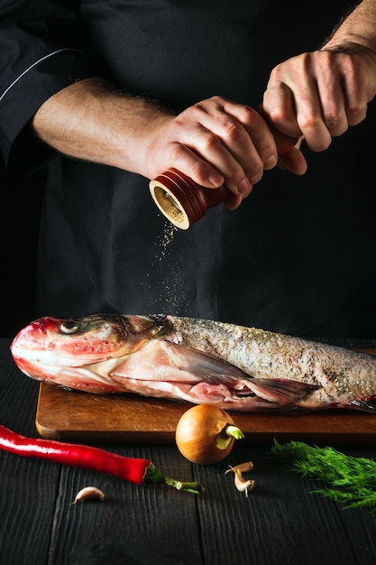 The chef prepares fresh fish bighead carp sprinkling pepper. Preparing to cook fish food. Working environment in the restaurant or cafe kitchen