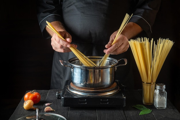 Chef prepares Italian pasta in saucepan with vegetables Closeup of cook hands while