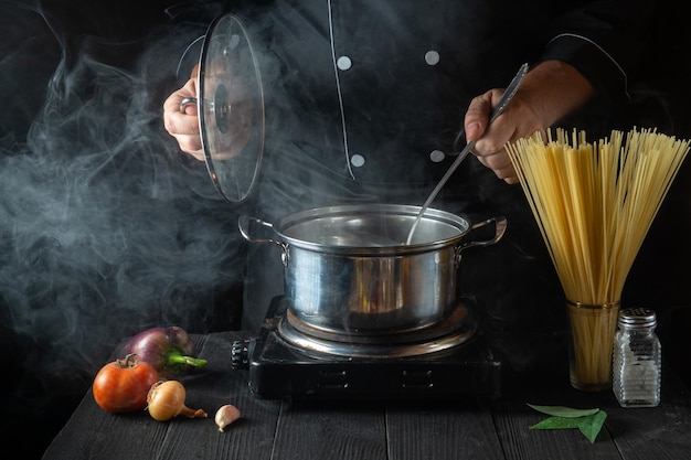 Chef prepares Italian pasta in a saucepan with vegetables