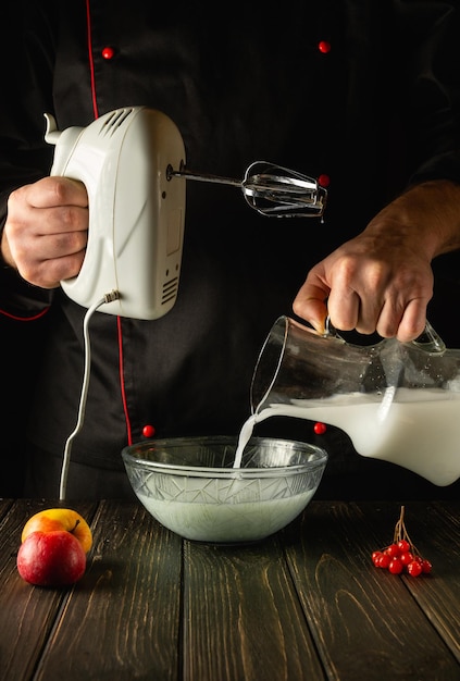 Шеф-повар готовит молочный коктейль с фруктами на кухне с помощью электрического ручного миксера.