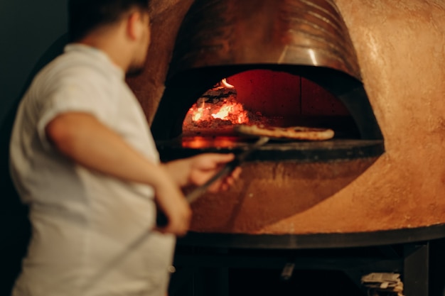 Foto lo chef prepara la pizza nel forno a legna. cucinare la pizza. il cuoco mette la pizza nel forno.