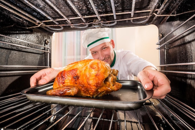 Шеф-повар готовит жареного цыпленка (сосредоточьтесь на курице) в духовке, вид изнутри духовки. Приготовление в духовке.