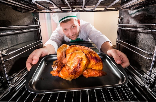 Chef prepares roast chicken (focus on chicken) in the oven, view from the inside of the oven. Cooking in the oven.