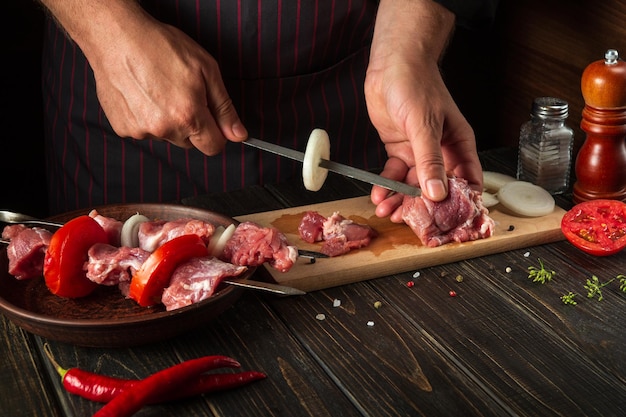 The chef prepares shish kebab with raw lamb meat and onions